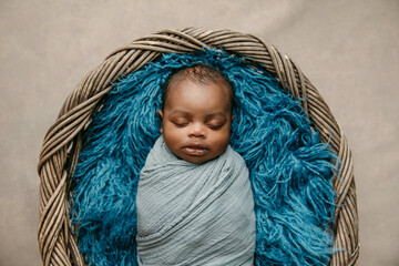 sleepy swaddled African-American newborn baby boy laying on a blue rug in a basket with copy space