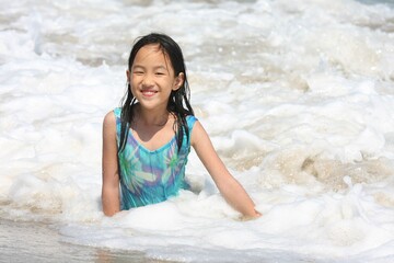 Young girl sit on beach surrounded by waves