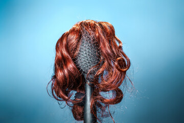 Females hair. Black hairbrush with a red wig, looks like a woman's head with a hairstyle. Blue background. Copy space. Concept of beauty salon, hair care and hair transplant