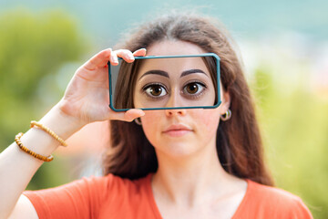 A woman closes her eyes with a smartphone, with a picture of huge cartoon eyes. The concept of hiding identity and fake pages in social networks