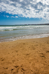 Nettuno, Lazio, Rome, Italy - The sea of the Roman coast, semi-deserted, at sunset. Cloudy blue sky in summer. The waves of the sea, slightly choppy. The beach, with sand and rocks.City in background