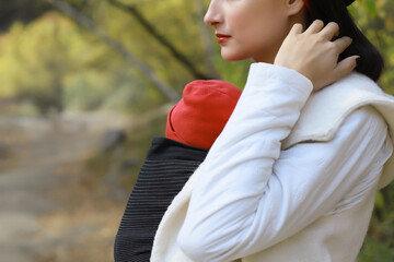 Beautiful young mother with her infant baby in sling outdoor. Woman is carrying her child and walk...
