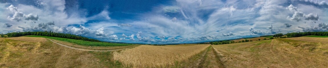 Panorama on some rural fields, with a blue sky and some clouds on it