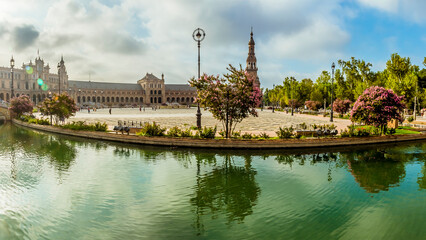 Fototapeta na wymiar A panorama view with reflections in the canals around the Plaza de Espana in Seville, Spain in the stillness of the early morning in summertime