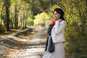 Beautiful young mother with her infant baby in sling outdoor. Woman is carrying her child and walk...