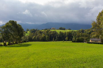 Summer landscape in the mountains. Beautiful lawn and house in mountains. Countryside landscape. Sunny field and mountains in clouds. Pasture and the village. Scenery valley. Farm in the hills.