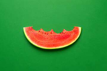 Slice of watermelon isolated on a green background. Bitten slice of watermelon top view.