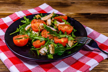 Roasted chicken breasts and salad with arugula and cherry tomatoes in a black plate