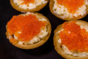 Tartlets with red caviar on a black plate. Festive food