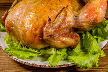 Plate with roasted whole chicken and lettuce leaves on a wooden table