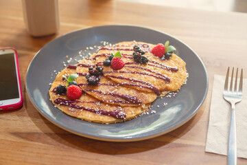Hot cake breakfast set with red berries on a wooden table with a cell phone on one side. Breakfast concept in the morning with natural light.