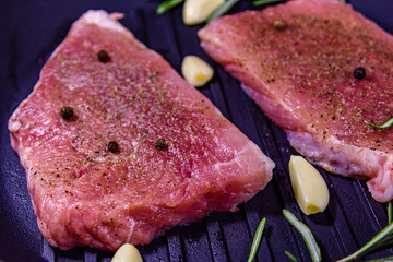 Raw steaks with garlic, rosemary and spices in a cast iron grill pan