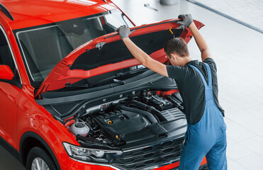 Top view of male worker in uniform that repairs red automobile