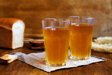 Summer soft drink. Two glass of homemade bread kvass with copy space. Beer with sackcloth on a wooden table with black rye bread hard chucks.