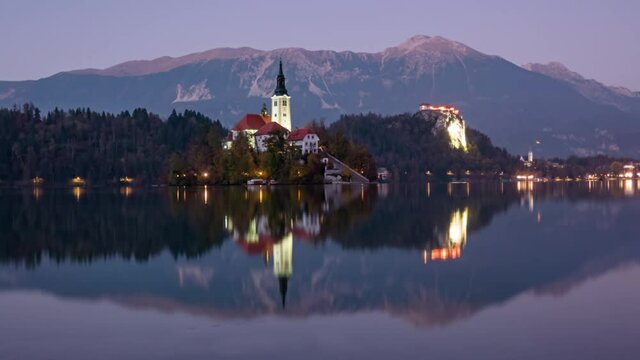 Day to night transition time lapse Bled Island (Blejski otok) with pilgrimage church of the Assumption of Mary and Bled castle on Lake Bled, Slovenia