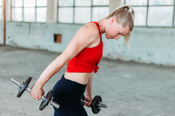 Fit blond woman weight lifting in red sportswear. Training, active lifestyle.