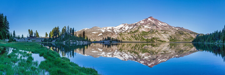 Mountain landscape with clear blue sky, morning light, reflective water, and a wide panoramic view.