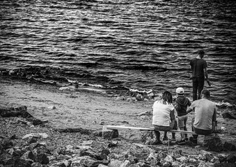 Russia, Saint-Petersburg - 26 July 2020: the family sits on a bench by the gulf of Finland and looks at the water, a man stands next to them and looks at the water in the same way