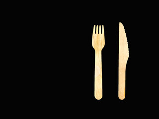 Wooden knife and fork isolated on a black background offset right. No people. Space for copy left