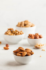 A handful of almonds in a white bowl, assorted nuts on a light background. Healthy snacks, healthy fats. Copy space.
