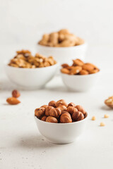 A handful of hazelnuts in a white bowl, assorted nuts on a light background. Healthy snacks, healthy fats. Copy space.