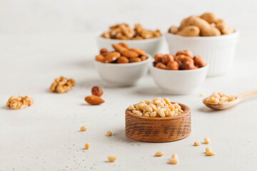 A handful of pine nuts in a wooden bowl, assorted nuts on a light background. Healthy snacks, healthy fats. Copy space.