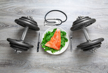 Raw salmon and baby spinach leaves on a plate between two weights