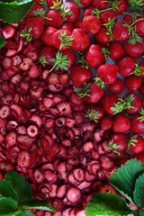 A large number of dried strawberry slices and whole fresh berries. Natural product. Dried strawberry fruit with green leaves. The background photo. Vertical photo.