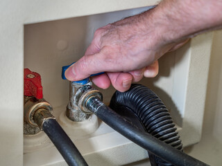 Plumber turning cold water supply shut-off valve for clothes washing machine.