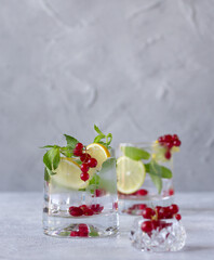 Two glasses of lemonade with lemon, fresh mint and red currant. Summer refreshment. Copy space, vertical orientation