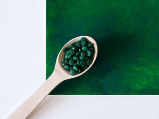 Green hawaiian spirulina in tablespoons pills in wooden spoon on green background. Super food, healthy lifestyle, healthy supplements, superfoods in cooking concept