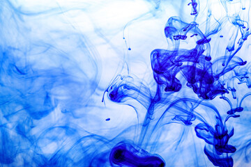 Blue ink injected into water from syringe, colour mixing with water creating abstract shapes