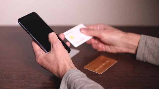 Online payment. Man's hands holding smartphone and using three different credit cards for online shopping