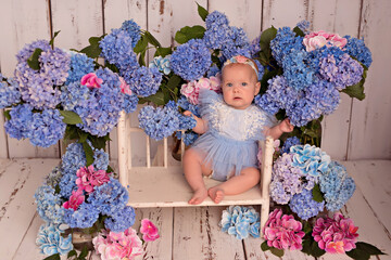Happy baby girl in a dress in the studio on a white background with pink and blue hydrangea flowers