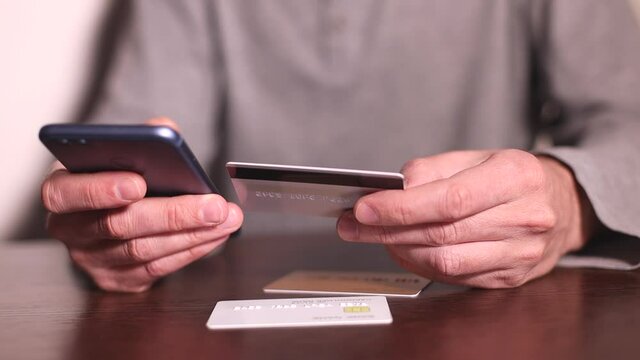 Online payment. Man's hands holding smartphone and using three different credit cards for online shopping
