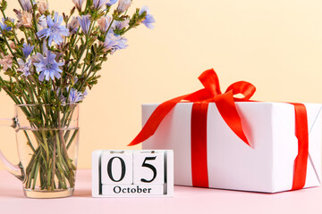 Flowers in a glass cup, gift and calendar with date of October 5, on a colored yellow pink...