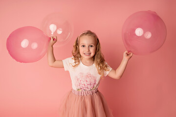 Happy baby girl on a pink background with balloons. Celebration. Birthday