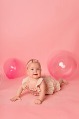 Happy baby girl on a pink background with balloons. Celebration. Birthday