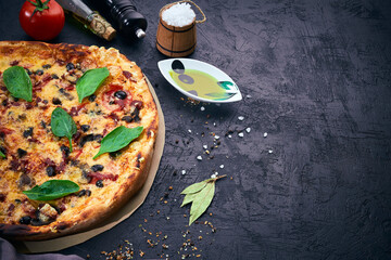 Homemade pizza and pizza cooking ingredients on dark background. Tomatoes, olives oil, herbs, salt...