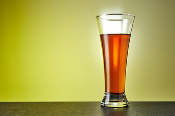 Tall glass of cold tea on warm yellow background. Fresh summer beverage.