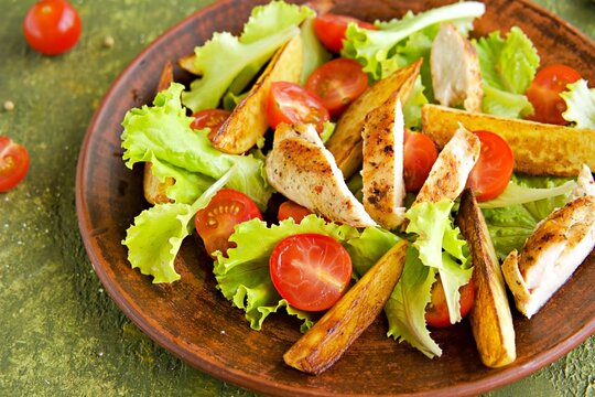 Warm salad with fried chicken fillet, lettuce and cherry tomatoes on a brown clay plate on an olive concrete background. Salad recipes..