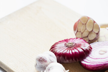 close up view of red onion and garlic on wooden cutting board isolated on white