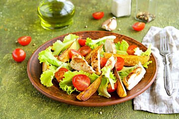 Warm salad with fried chicken fillet, lettuce and cherry tomatoes on a brown clay plate on an olive concrete background. Salad recipes..