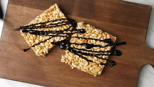 Pouring of chocolate sauce onto crispy rice bar on table, closeup