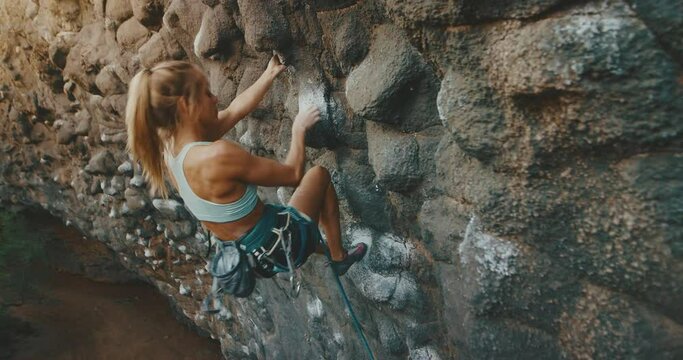 Strong young woman rock climbing up cliff, active healthy lifestyle