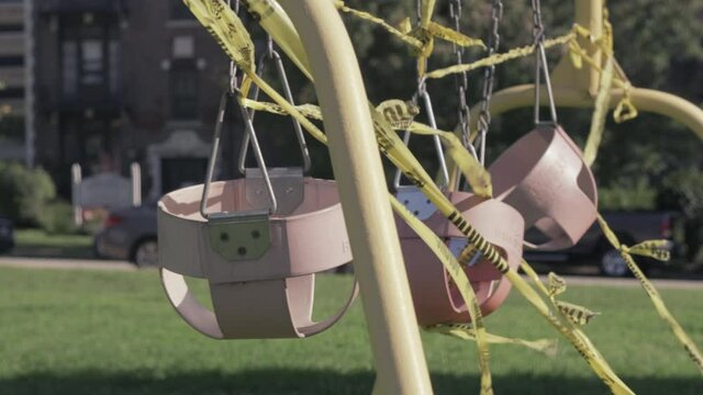 Static shot of swing set with caution tape wrapped around it on sunny day