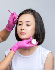 Brunette teenager girl having permanent makeup tattoo on her eyebrows. Make-up artist makes...