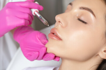 Woman with beautiful clean skin. Cosmetologist does injections for lips augmentation and anti...