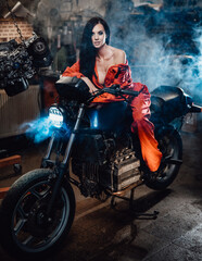 Sexy looking women in work overalls sitting on a black motorcycle in a car service