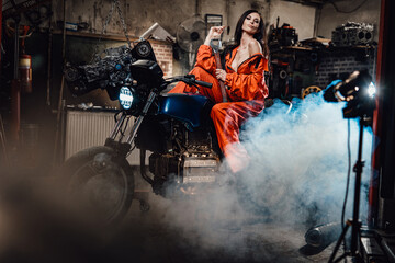 Sexy looking brunette in work orange overalls sitting on a black motorcycle in a car service